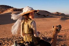 a woman riding on the back of a camel in the desert with a scarf around her head