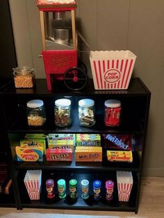 an assortment of snacks and popcorn on a shelf in front of a popcorn machine,