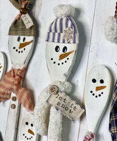 snowman spoons are hanging from hooks on a white wooden wall, decorated with ribbons and tags