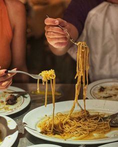 two people eating spaghetti from white plates on a table