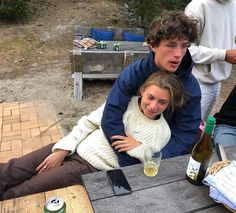 two people sitting at a picnic table with bottles of wine and beer in front of them