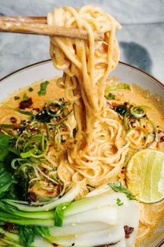 a bowl filled with noodles and vegetables on top of a marble countertop next to chopsticks