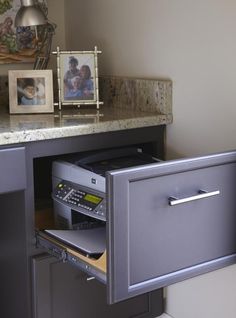 an open file cabinet next to a desk with pictures on it and a phone in the drawer