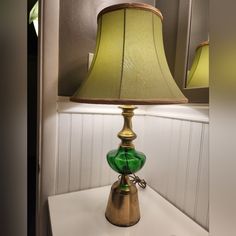 a green glass lamp sitting on top of a white table next to a framed mirror