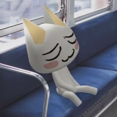 a white cat sitting on top of a blue seat next to a window with its eyes closed