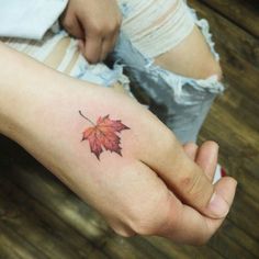 a woman's hand with a small red leaf tattoo on her left wrist and the other arm