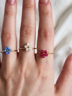 a woman's hand with three different colored flowers on it and two gold rings