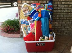 a red cooler filled with lots of items on top of a sidewalk next to a brick wall