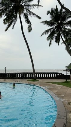 people are swimming in an outdoor pool next to the ocean with palm trees on either side