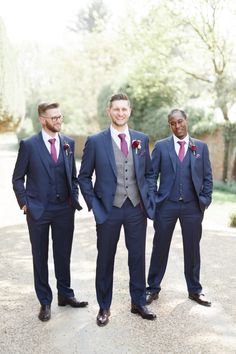 three men in suits standing next to each other on a gravel road with trees in the background