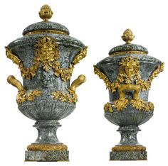 two large vases sitting next to each other on top of a white surface with gold decorations