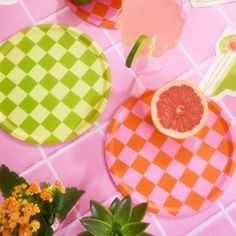 grapefruits and orange slices are sitting on checkered paper plates with flowers in vases