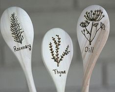 three wooden spoons with different types of flowers and leaves on them, one has the word rosemary written on it