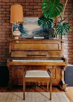 a grand piano in front of a painting on a brick wall with a bench and lamp