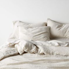 an unmade bed with white sheets and pillows