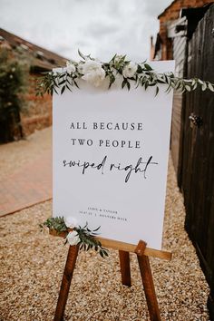 a wedding sign with greenery and flowers on it sitting in the middle of gravel