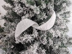 a white ribbon is tied to the top of a christmas tree with snow on it