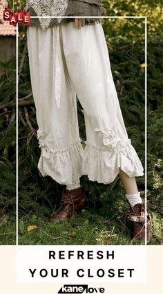 a woman standing in the grass with her legs crossed wearing white pants and brown boots