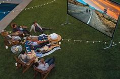 people sitting on lawn chairs in front of an outdoor movie screen with lights strung across the grass