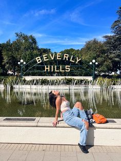 a woman laying on the edge of a fountain in front of beverly hills entrance sign