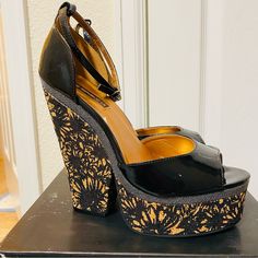 Beautiful Black Patent Wedge On A Cork Wedge With Black Flower Stamp Print And Gold Accents And Ankle Straps. Some Cracking On The Patent Of One Shoe But They Were Never Worn Out. Sky High 6 In. Heel With A 2 In. Platform. These Do Come With The Original Box. Please See Photos For Approximate Measurements. Wedge Sandals With 4-inch Heel For Night Out, Black Synthetic Wedge Sandals For Party, Black Platform Wedge Sandals For Evening, Black Sandals With 4-inch Wedge Heel, Wedge Heel Sandals For Night Out, Party Wedge Sandals With 4-inch Heel, Spring Night Out Wedge Sandals, Black Wedge Sandals For Night Out With Closed Toe, Black Ankle Strap Wedge Sandals For Party