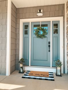 a blue front door with a welcome mat and two lanterns on the side of it