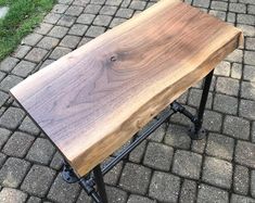 a small wooden table sitting on top of a brick road next to grass and trees