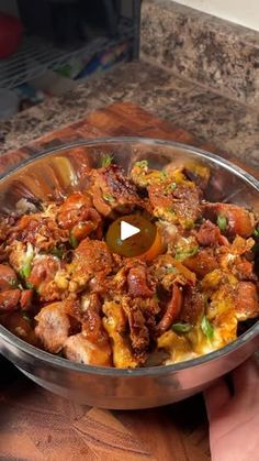 a person holding a metal bowl filled with food on top of a wooden countertop