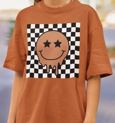 Comfort Colors® Smiley Face Tee Collection: Checkered Smiley Face Crafted from premium 100% ring spun cotton by Comfort Colors, these shirts guarantee comfort and durability. For best results, wash on cold and hang to dry. This Comfort Colors Tee comes in standard unisex sizing. For a more oversized fit, consider sizing up. For those aiming for an oversized "T-shirt Dress" vibe, we recommend going up 2 sizes. Please consult the size chart to ensure the perfect fit for you. If you don't see the color that you want, message us to see if we can make it happen Rest assured, a tracking number will be provided once your order is shipped. Should you encounter any issues or have questions, please don't hesitate to reach out. Your satisfaction is our top priority! Please note: Due to the direct-to- Brown Cotton Top With Graphic Design, Brown Crew Neck Graphic Tee Shirt, Brown Crew Neck Graphic Tee, Brown Crew Neck T-shirt With Logo Print, Casual Brown Top With Graphic Design, Brown Cotton Graphic Design T-shirt, Brown Cotton T-shirt With Logo Print, Brown Graphic Tee With Logo Print, Brown Graphic Tee With Graphic Design