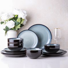 black and white dinnerware set with flowers in vase on countertop next to wall