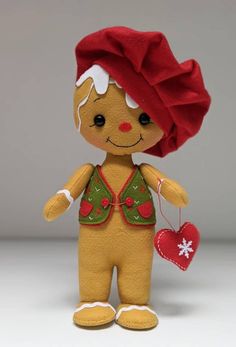 a small stuffed doll with a red hat and green shirt holding a heart ornament