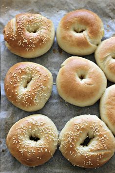 six bagels with sesame seeds are on a piece of wax paper