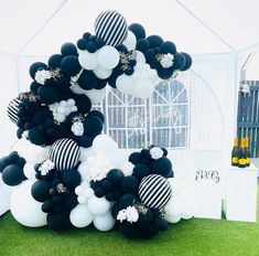 black and white balloons are arranged in the shape of a house on grass with a fence behind it