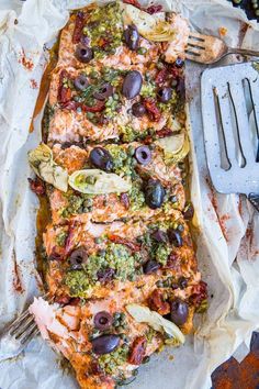 an entree with olives, broccoli and other toppings on a sheet of parchment paper