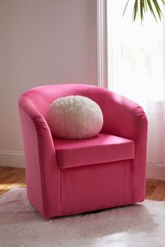 a pink chair with a fluffy white pillow on it's back in front of a window