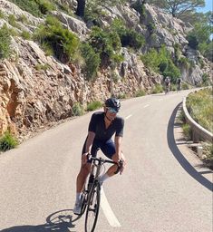 a man riding a bike down a road next to a rocky cliff face covered in greenery