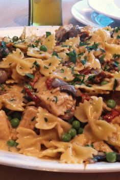 a white plate topped with pasta covered in sauce and peas next to a glass of beer