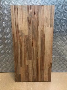 a wooden cutting board sitting on top of a tile floor next to a metal wall