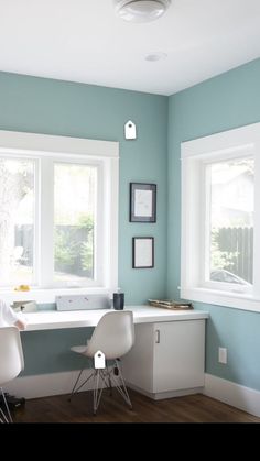 two white chairs sitting in front of a window next to a desk with a computer on it