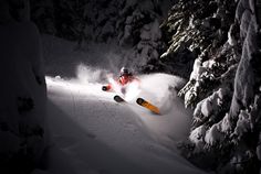 a person riding skis down a snow covered slope at night in the mountainside