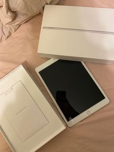 an open box sitting on top of a bed next to a white tablet computer and its packaging