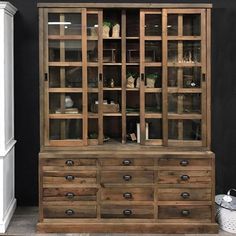 a large wooden cabinet with glass doors and drawers on the bottom, in front of a black wall