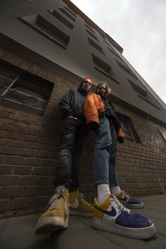 two people sitting on the side of a building with their arms around each other's legs