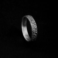 a silver ring with intricate designs on it's side, against a black background