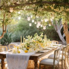 an outdoor dining table set up with white and yellow flowers, candles and lemons