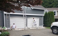 two men are painting the side of a house in front of a white truck and ladder