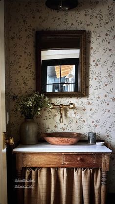 a bathroom sink sitting under a mirror next to a wall papered wall with flowers on it