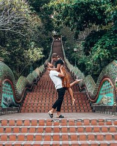 a man and woman are dancing on the steps in front of some green trees,