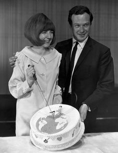 a man and woman standing next to each other in front of a cake