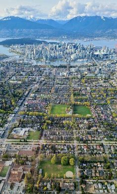 an aerial view of a large city with mountains in the back ground and trees on both sides